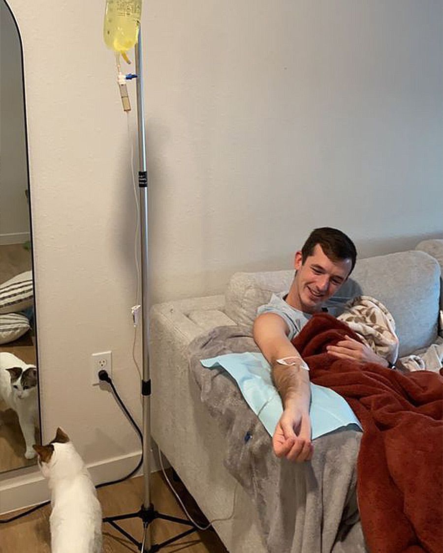 Comfortable mobile IV therapy for wellness or recovery at home, showing a happy patient and his curious cat.