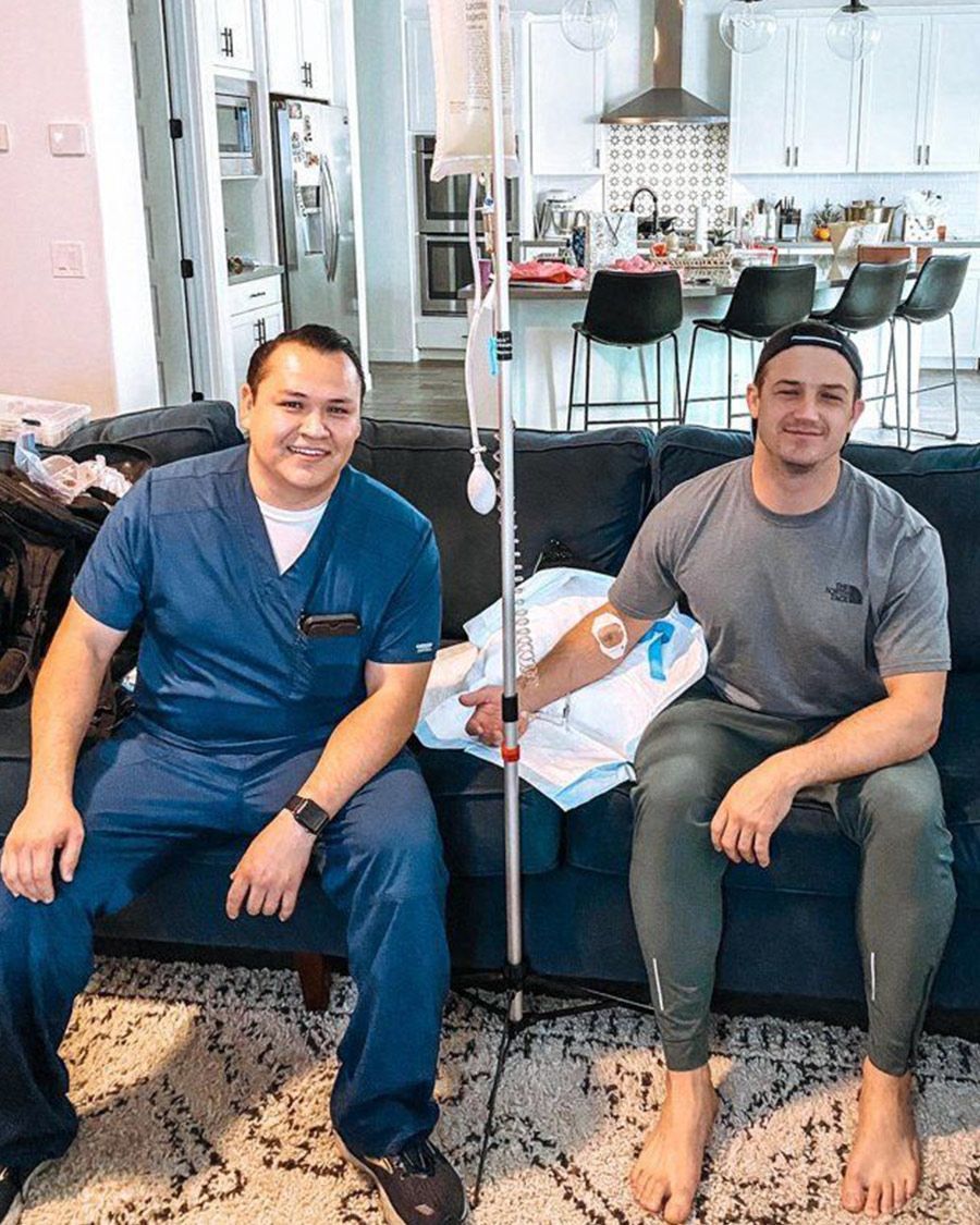 At-home mobile IV therapy service with a medical professional and a happy male client in a residential living room.