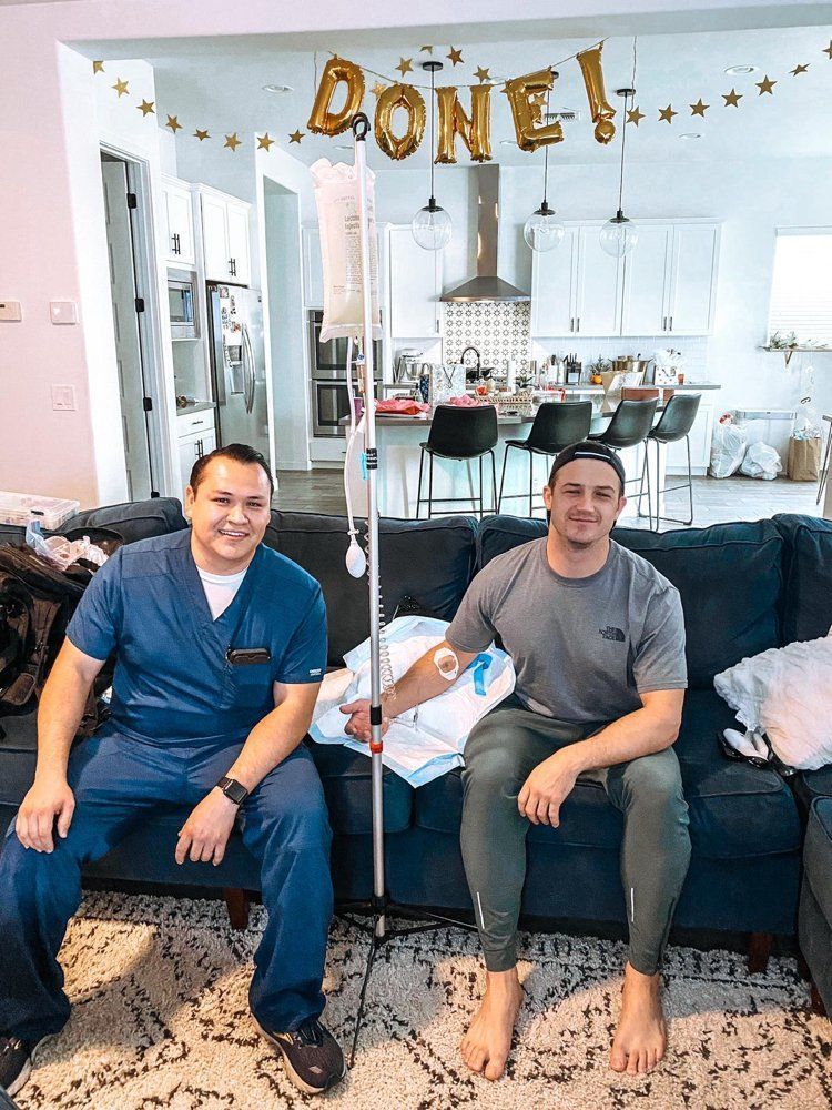 Two men are sitting on a couch in a living room with balloons that say done.