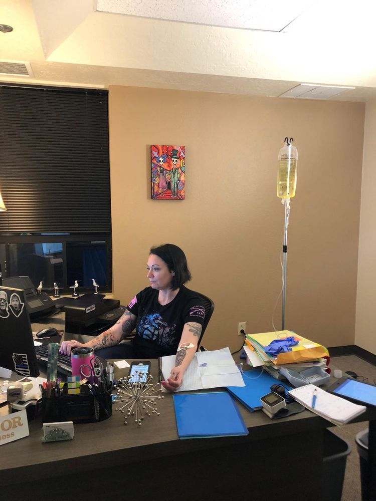 A woman is sitting at a desk with an iv in her hand.