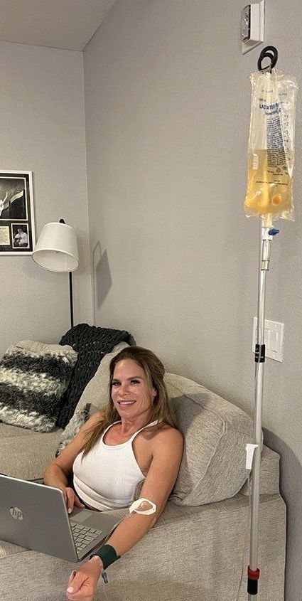 A woman is sitting on a bed with a laptop and an iv in her arm.