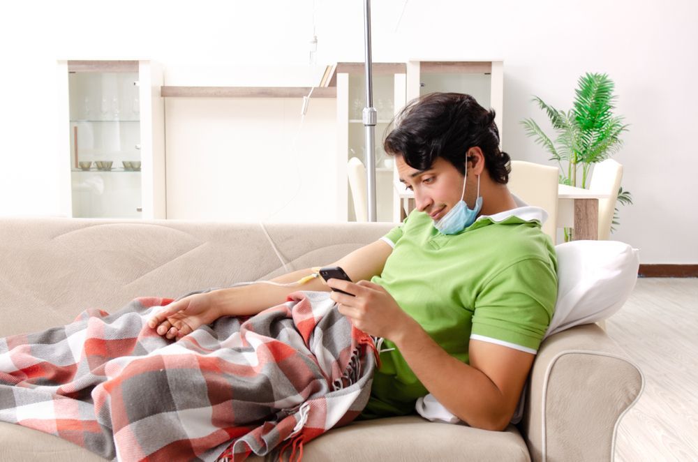 A man is laying on a couch wearing a mask and using a cell phone.