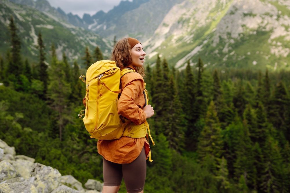 A woman with a yellow backpack is standing on top of a mountain.