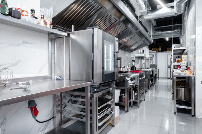 Commercial kitchen with stainless steel appliances, ventilation hood, and bright lighting.