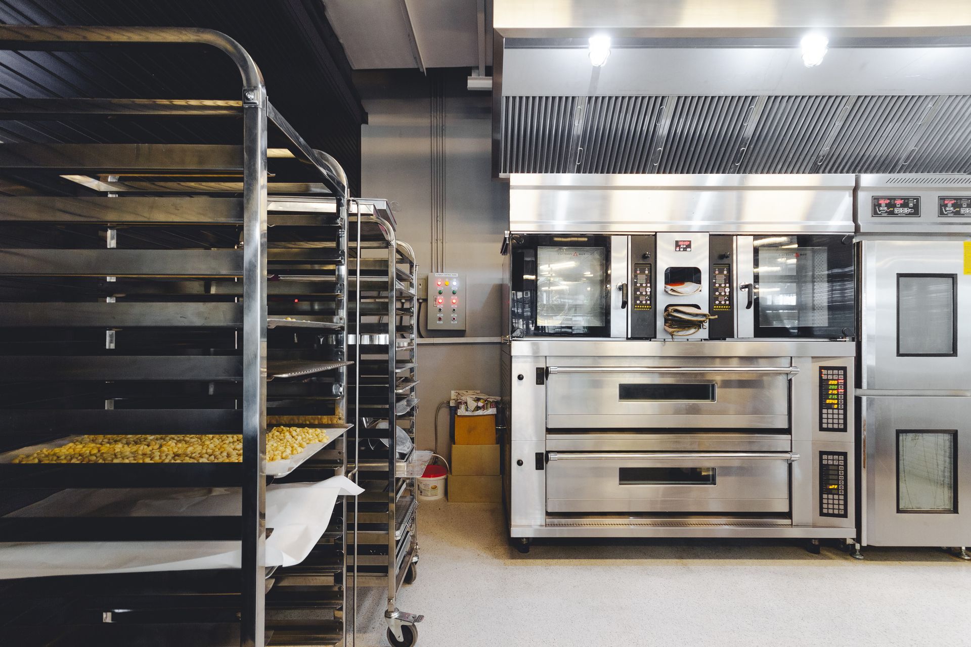 Stainless steel commercial ovens in a bakery, next to a rack of trays.