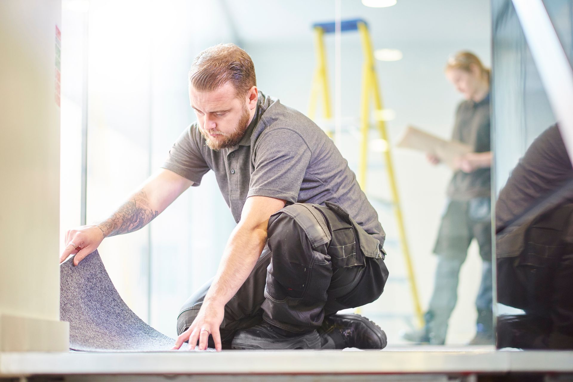 Technician kneeling on floor performing professional carpet fixing in modern office hallway.