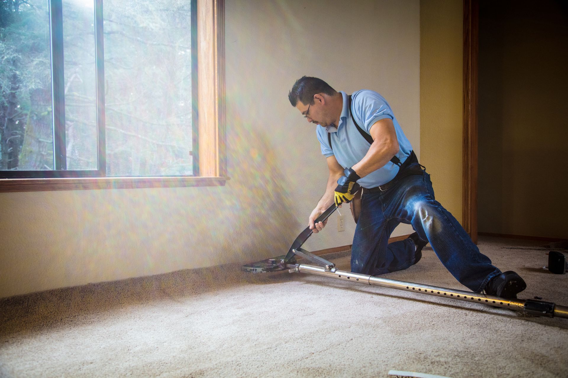 Professional installer using carpet stretching tools during home carpet repair.