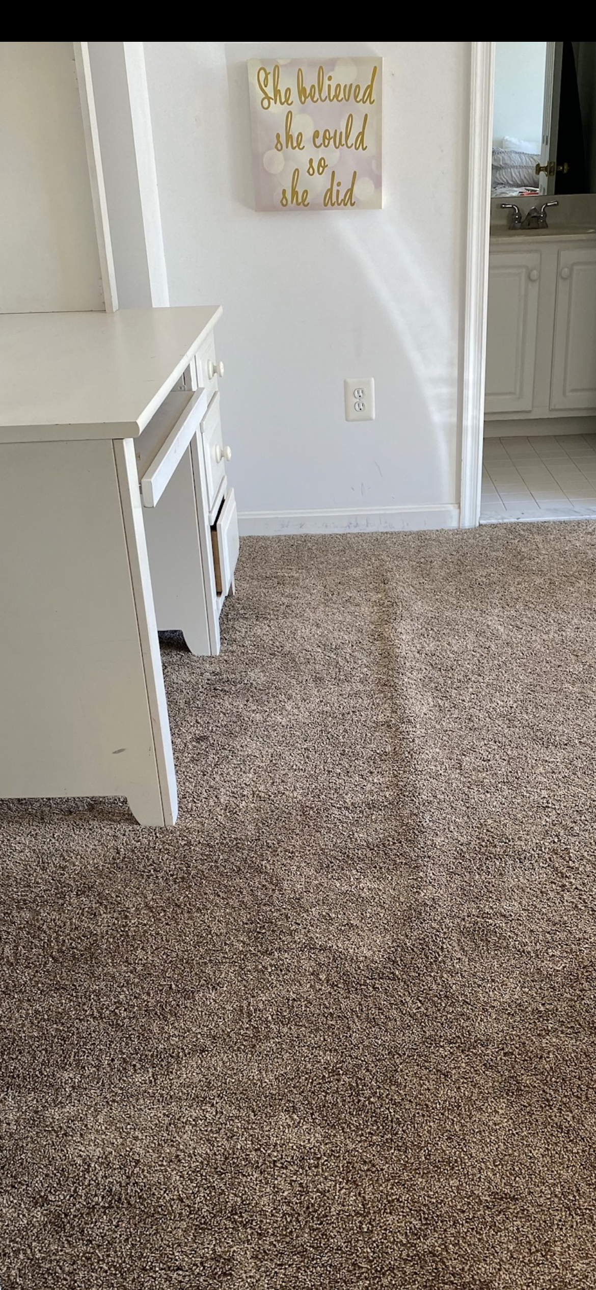 White desk in a room with brown carpet. A sign that reads 