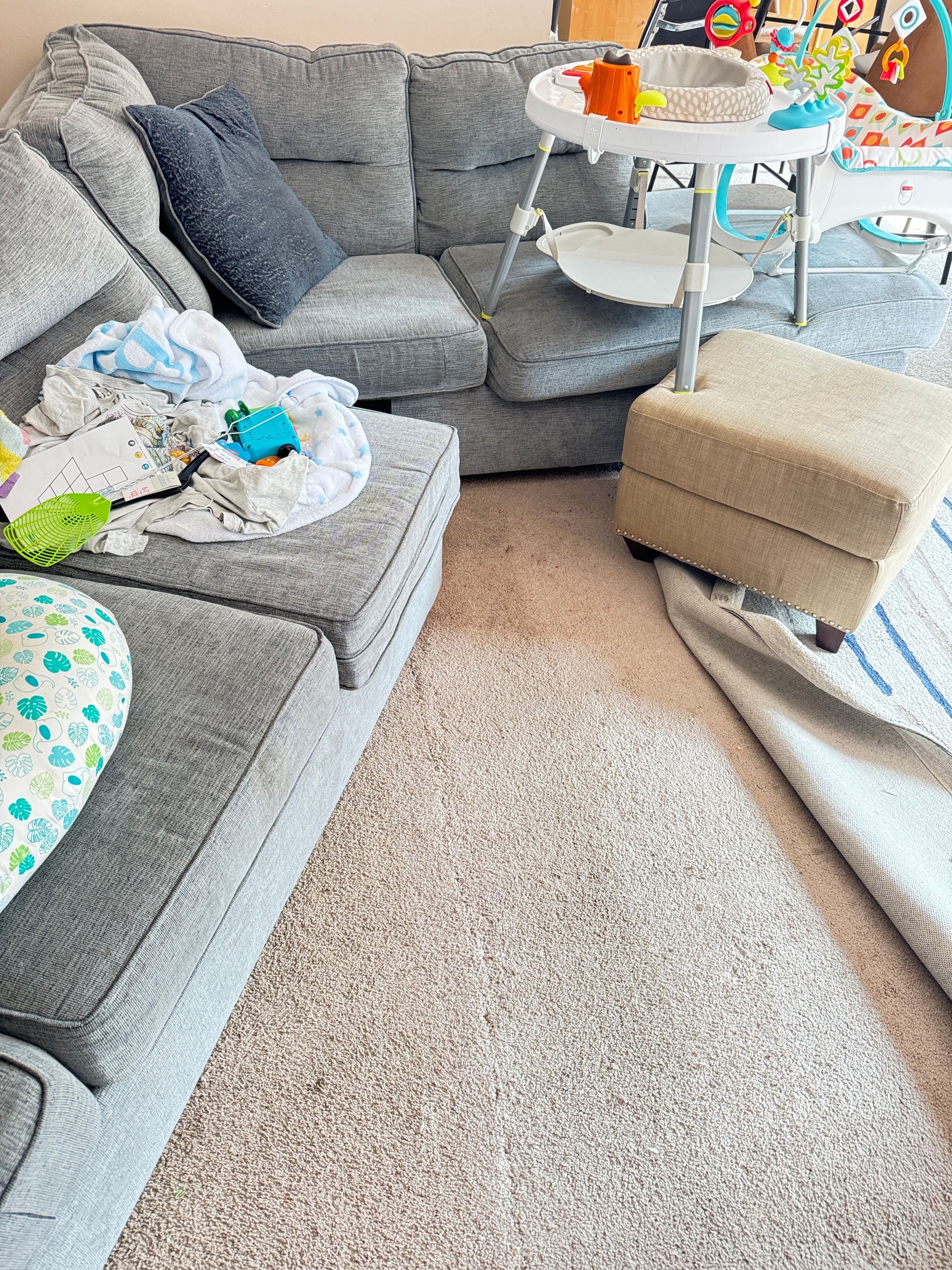 Gray sectional sofa in a living room with baby items.