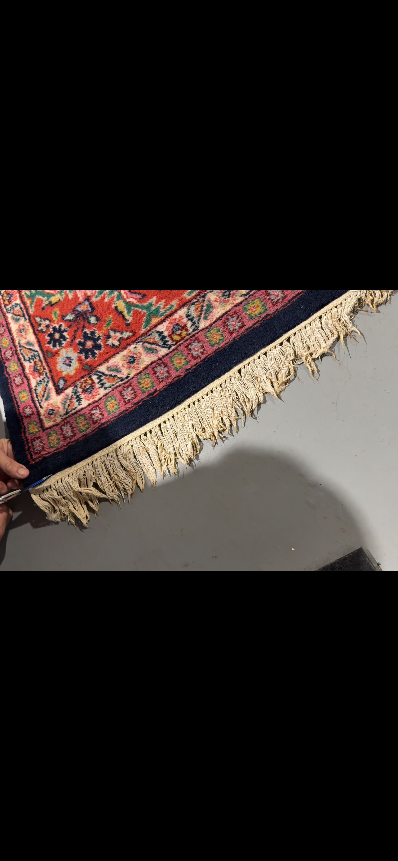 A close-up of a rug with intricate patterns and fringe, on a gray surface.
