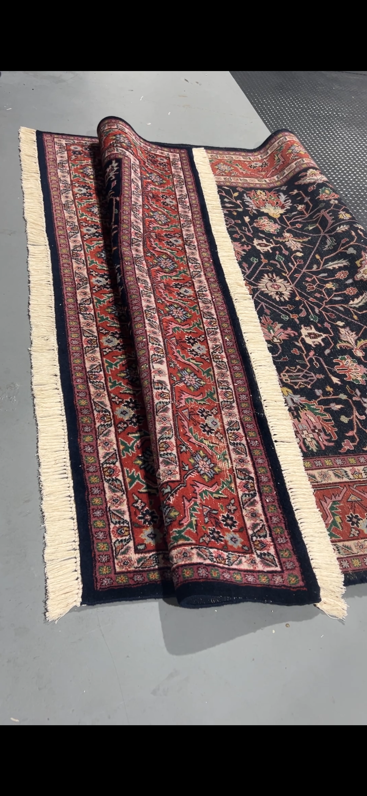 Rolled red and navy carpet with fringed edges on a gray surface.