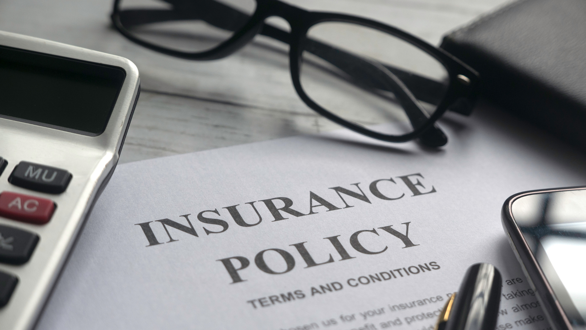 Insurance policy document with calculator, glasses, and phone.