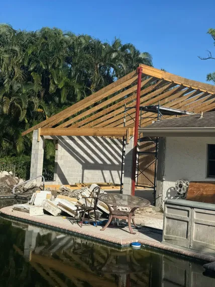 A house with a wooden roof is being built next to a pool.