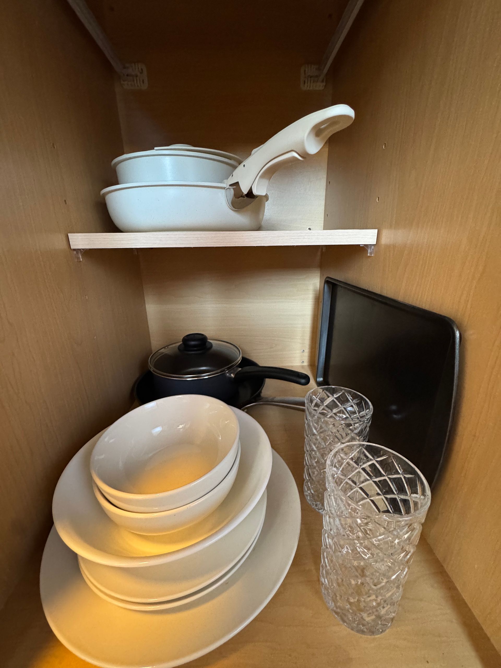 A cabinet with cookware, dishes, and glasses on shelves.