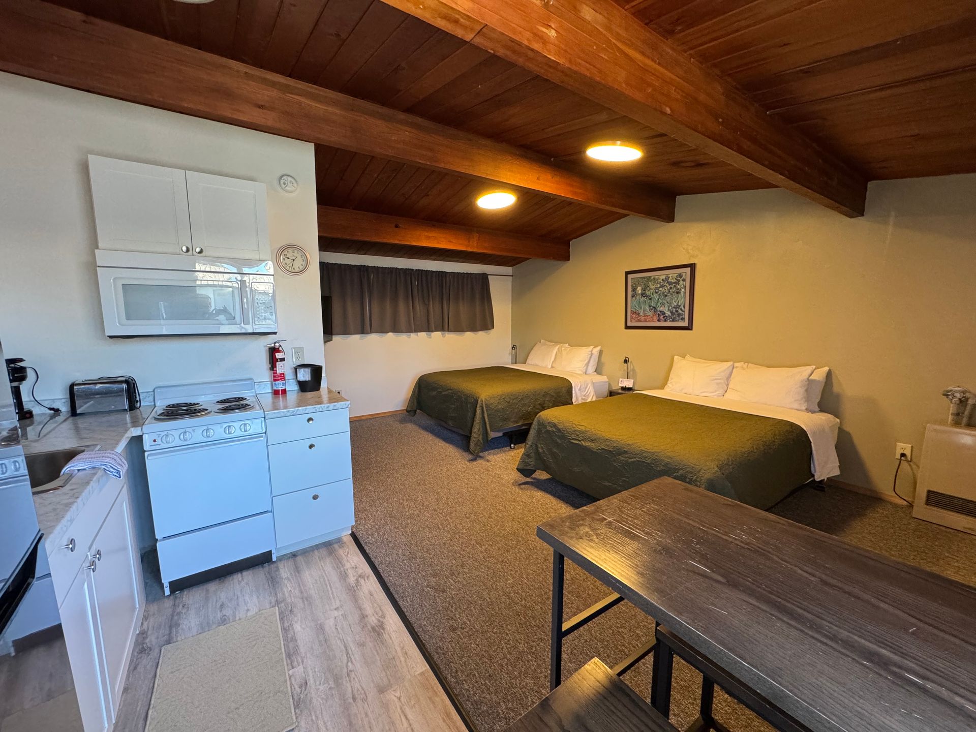 Studio apartment with two beds, small kitchen, wooden table, and exposed beam ceiling.