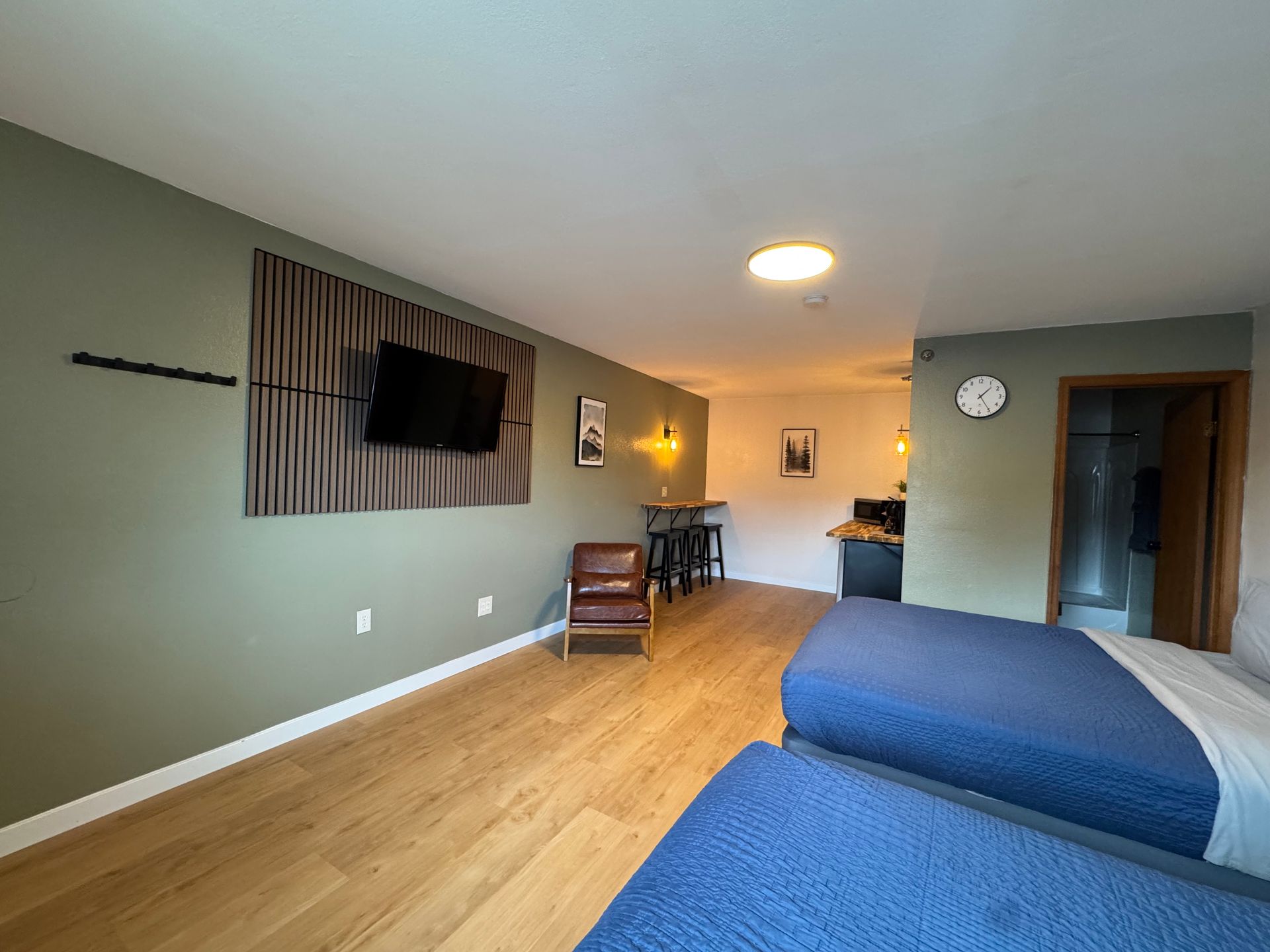 Studio apartment with two beds, a TV, a small table, and a chair; green walls, wooden floor.