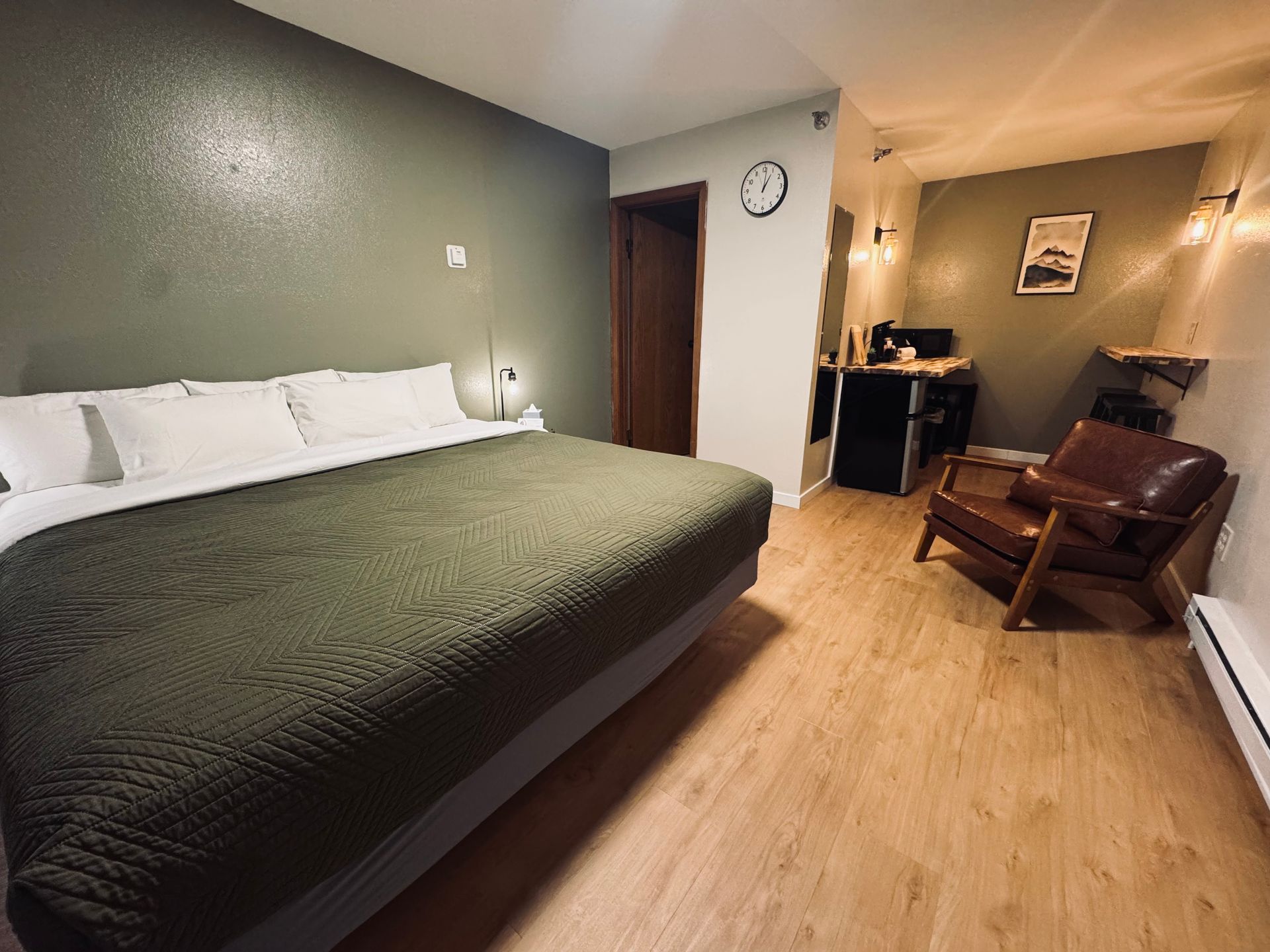 Bedroom with queen bed, olive green accents, leather armchair, and a work desk.