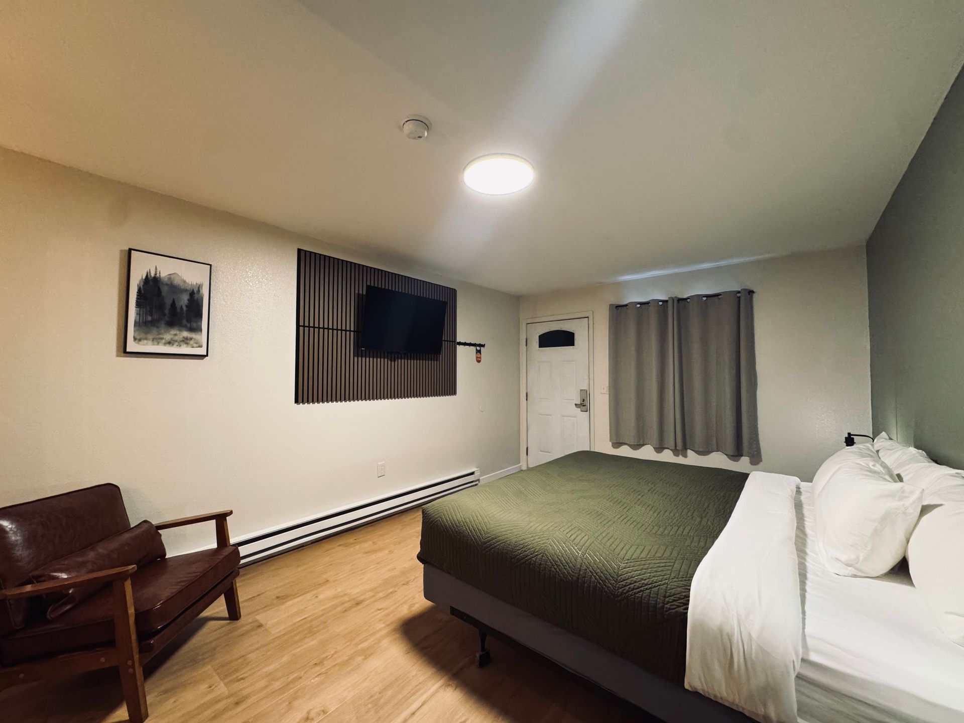A motel room with a bed, TV, chair, and a picture on the wall.