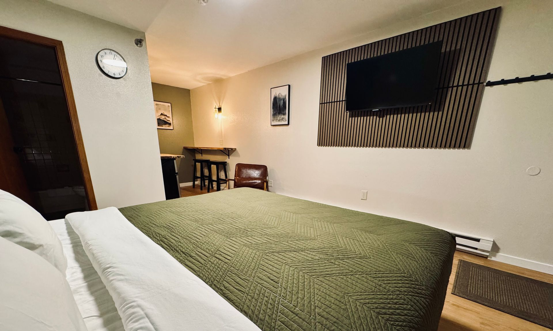Bedroom with a bed, TV, and small table; earth tones with a green bedspread.