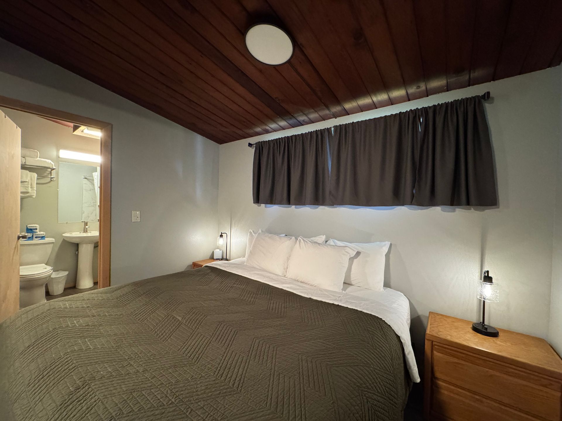 Bedroom with a bed, nightstands, dark curtains, and an attached bathroom.