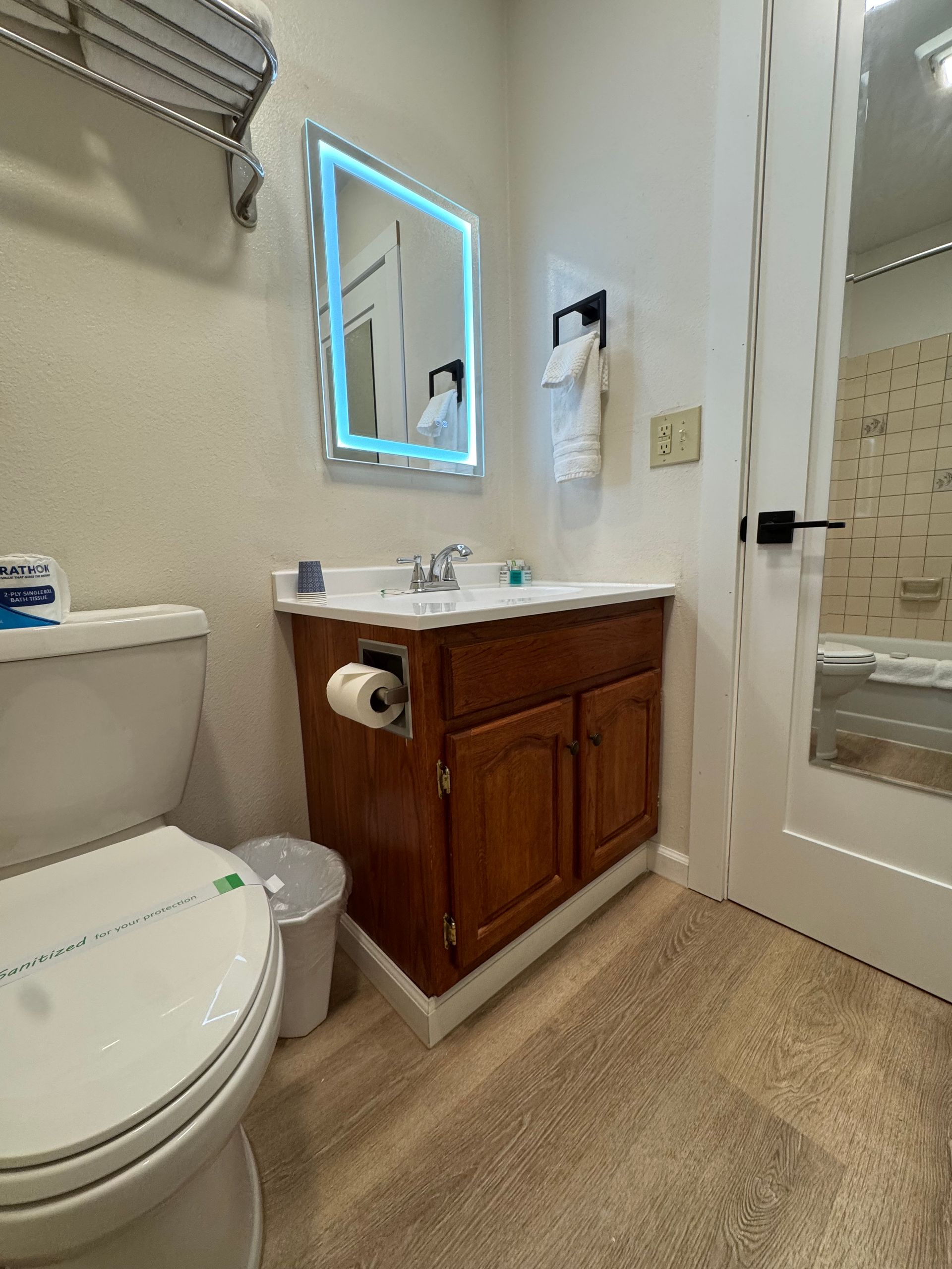 Bathroom with toilet, vanity, mirror, towel rack, and open door.