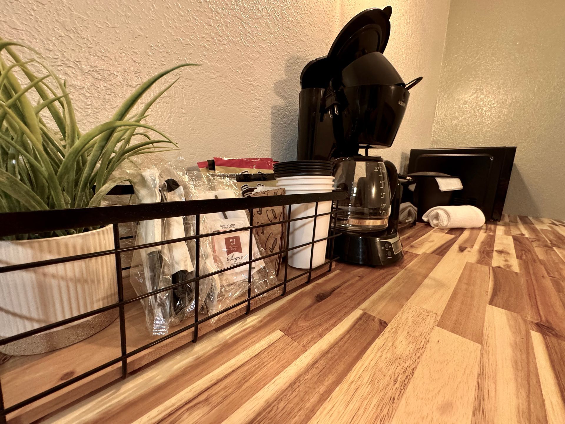 Coffee station with black coffee maker, wire rack, plant, on wood counter.