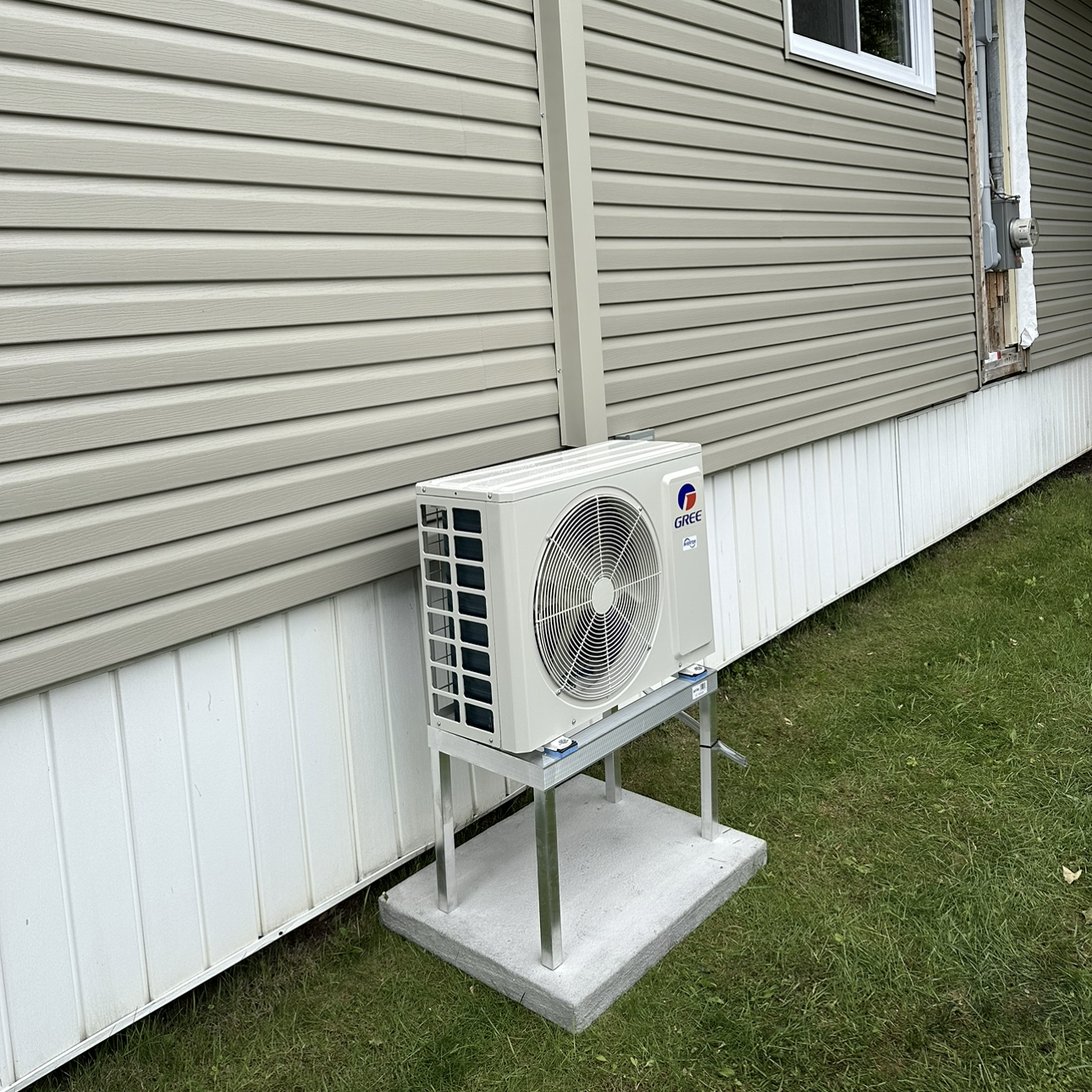 Un climatiseur blanc est posé sur une plate-forme en béton à côté d'une maison.