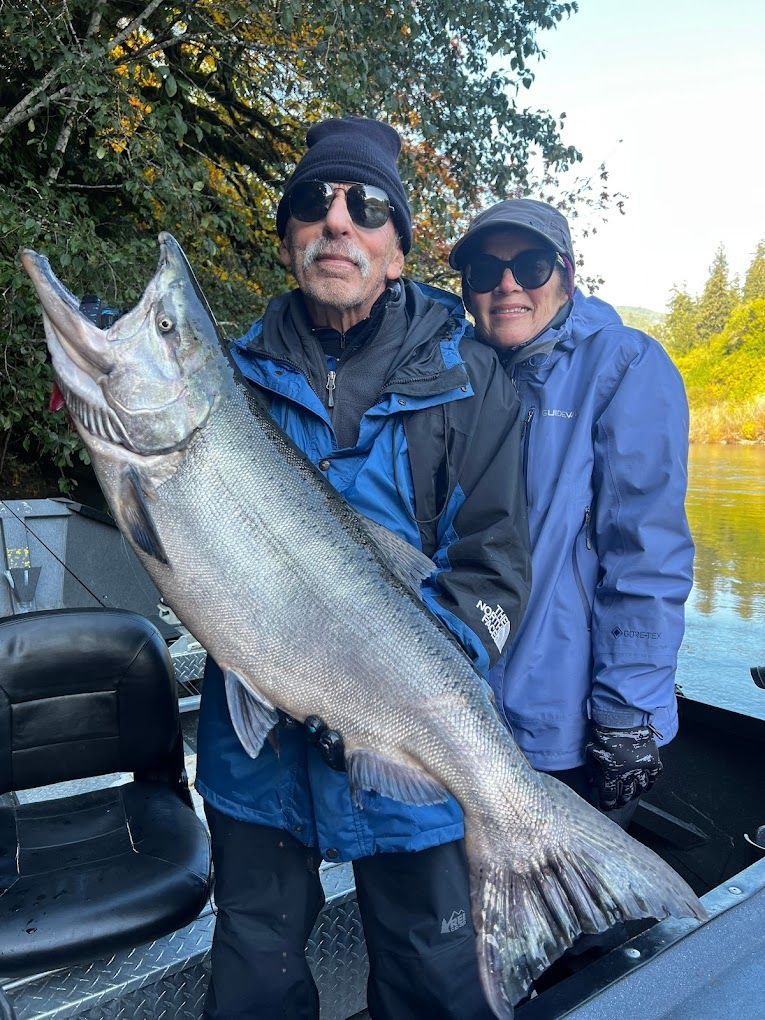 A man and a woman are standing next to a boat holding a large fish.