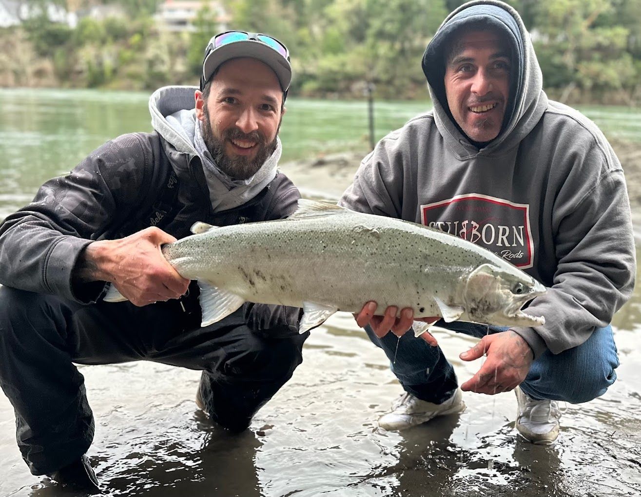Two men are kneeling down in the water holding a large fish.