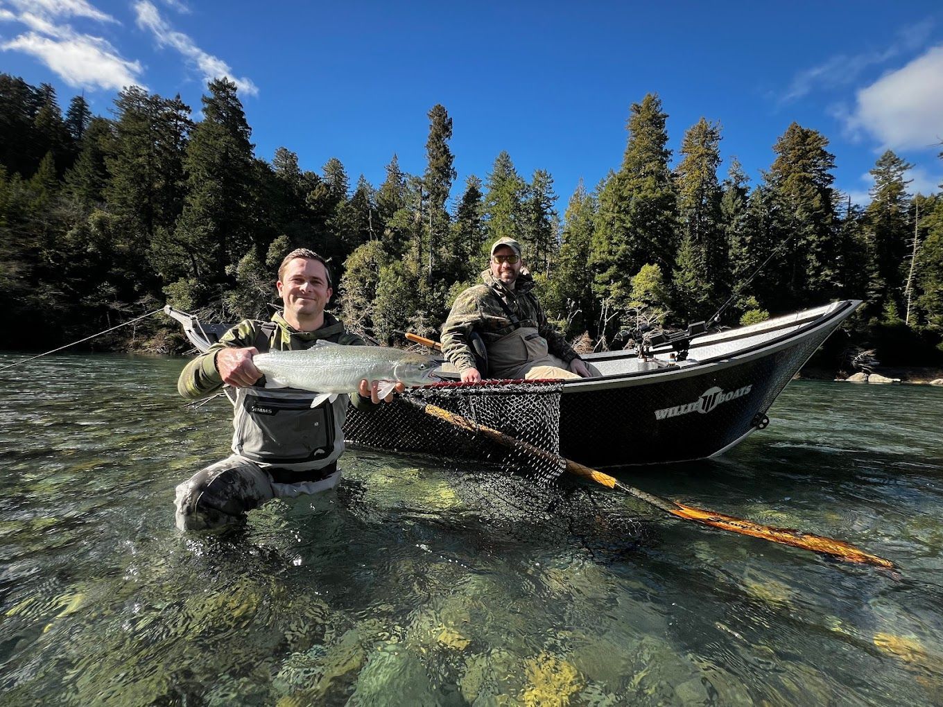 A man is kneeling in the water holding a fish next to a boat.