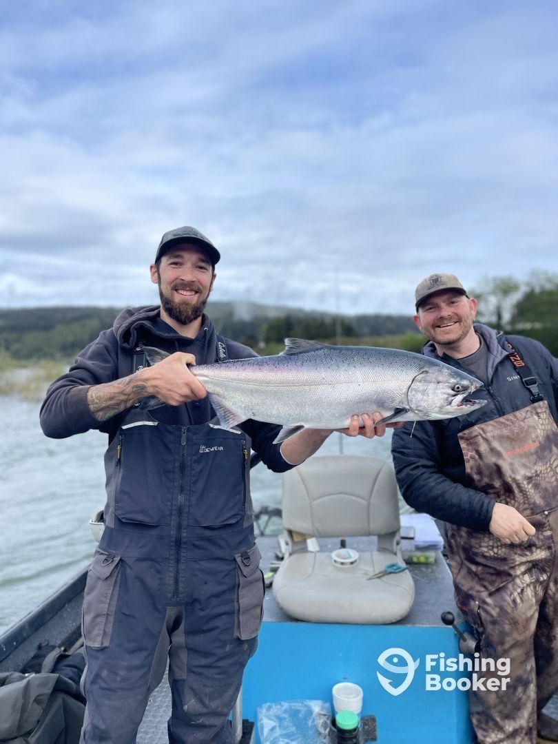 Two men are standing on a boat holding a large fish.