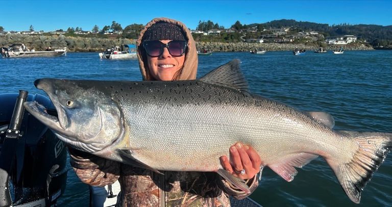 A woman is holding a large salmon in her hands on a boat.