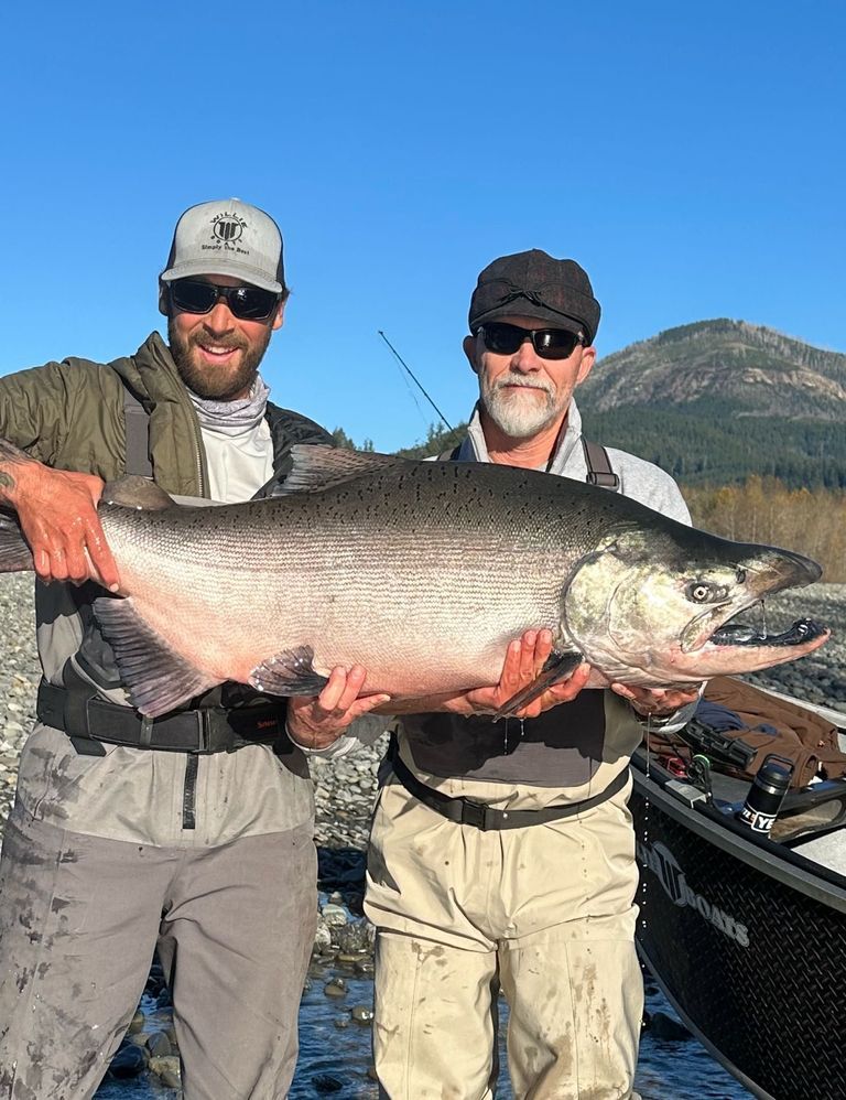 Two men are holding a large salmon in their hands.