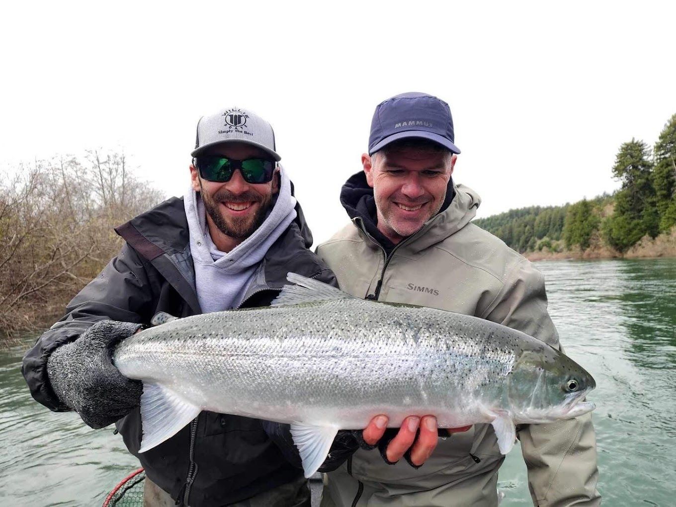 Two men are holding a large fish in front of a river.