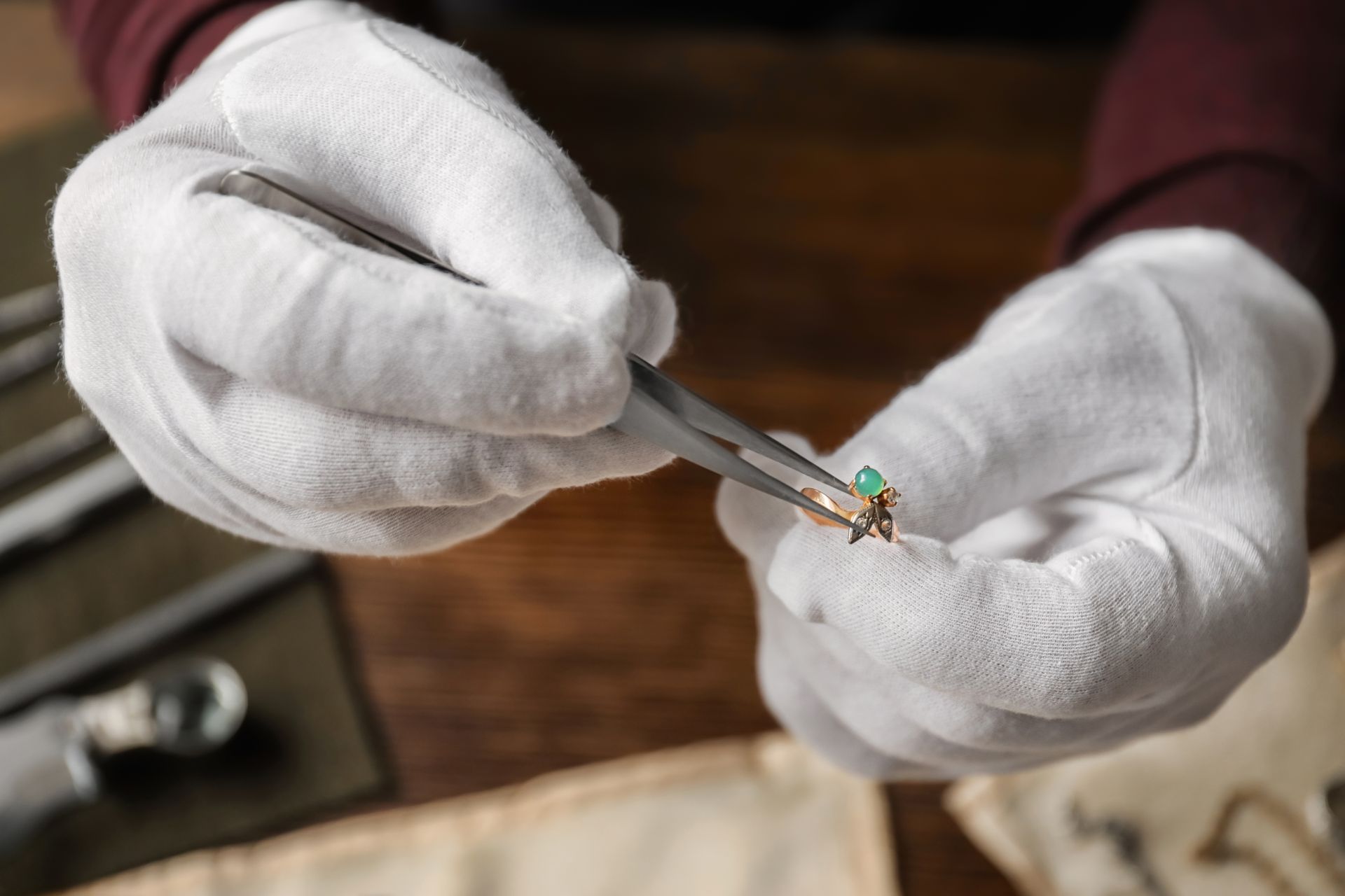 A person wearing white gloves is holding a ring with tweezers.