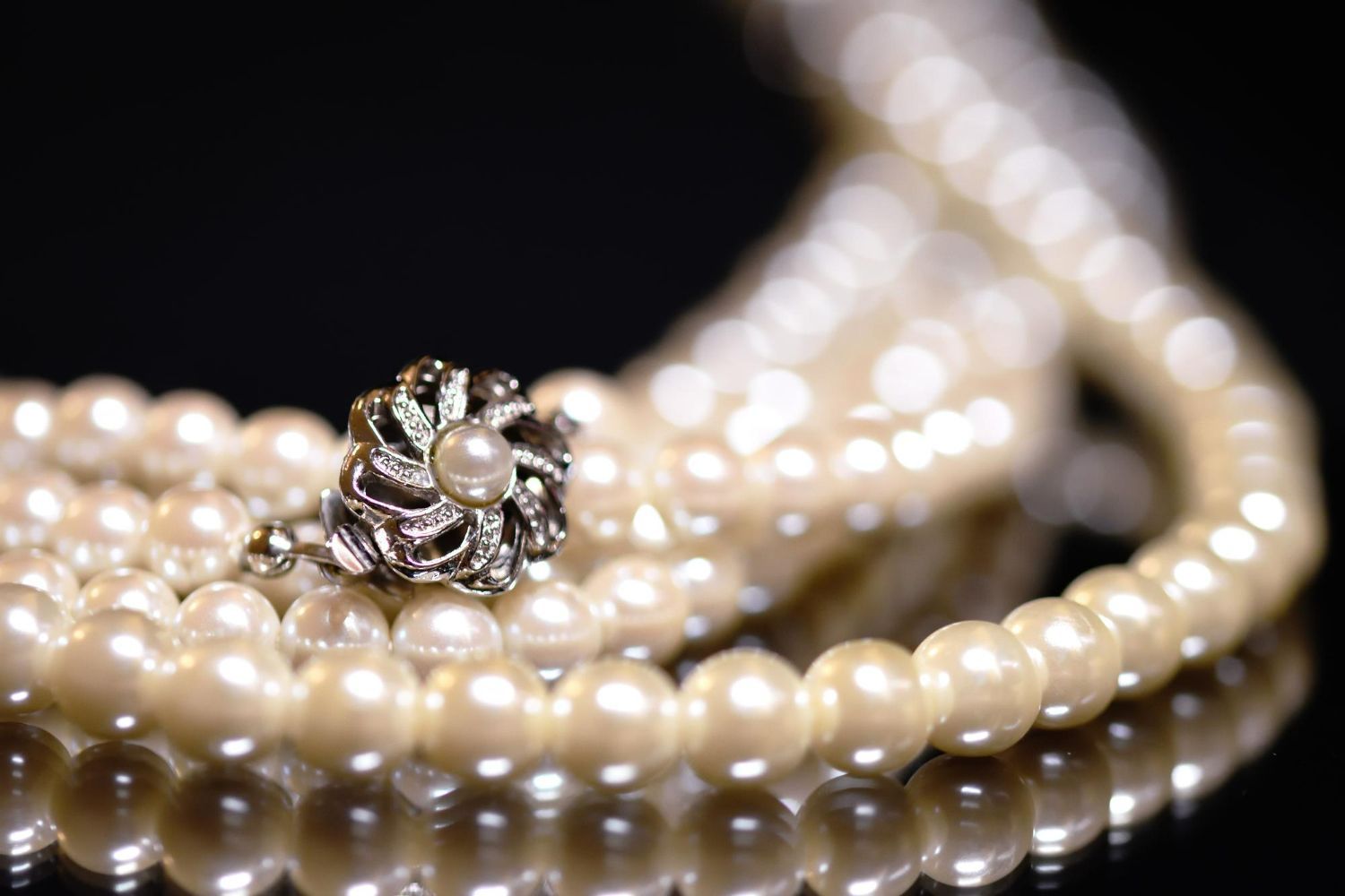 Pearl necklace with decorative clasp resting on a reflective black surface.