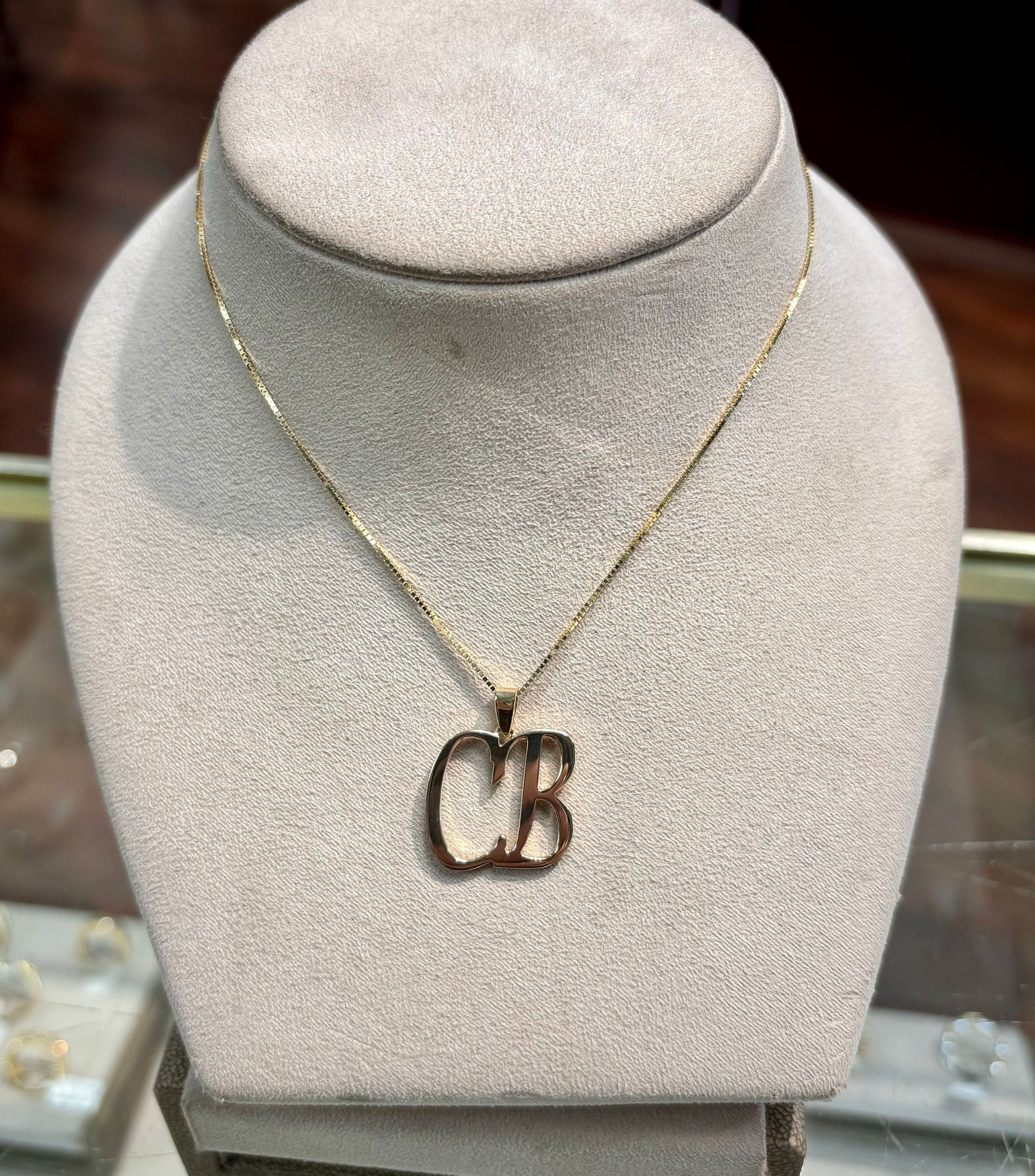 A necklace with the letter cb on it is on a mannequin.