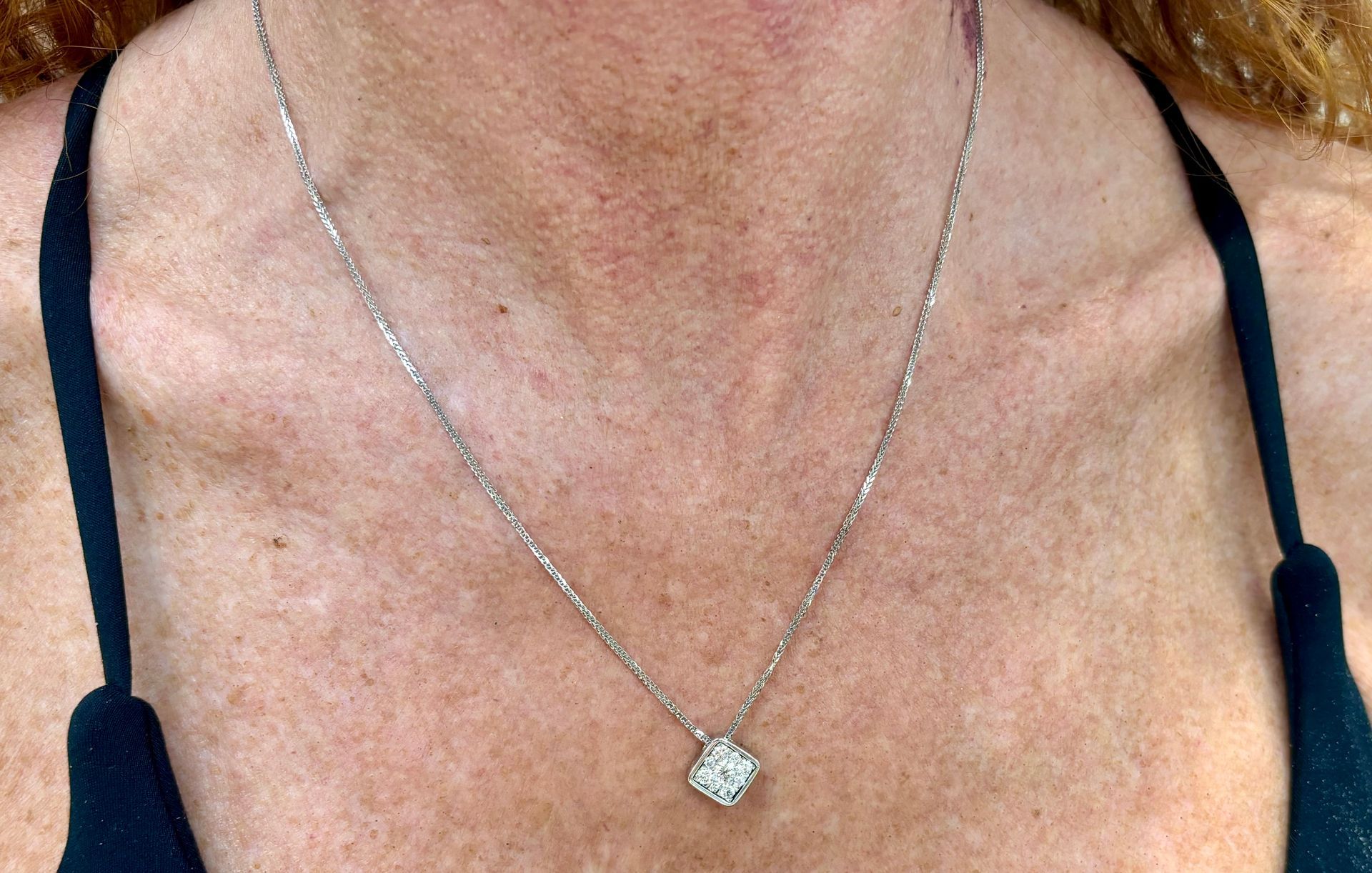 A woman is wearing a necklace with a diamond pendant.