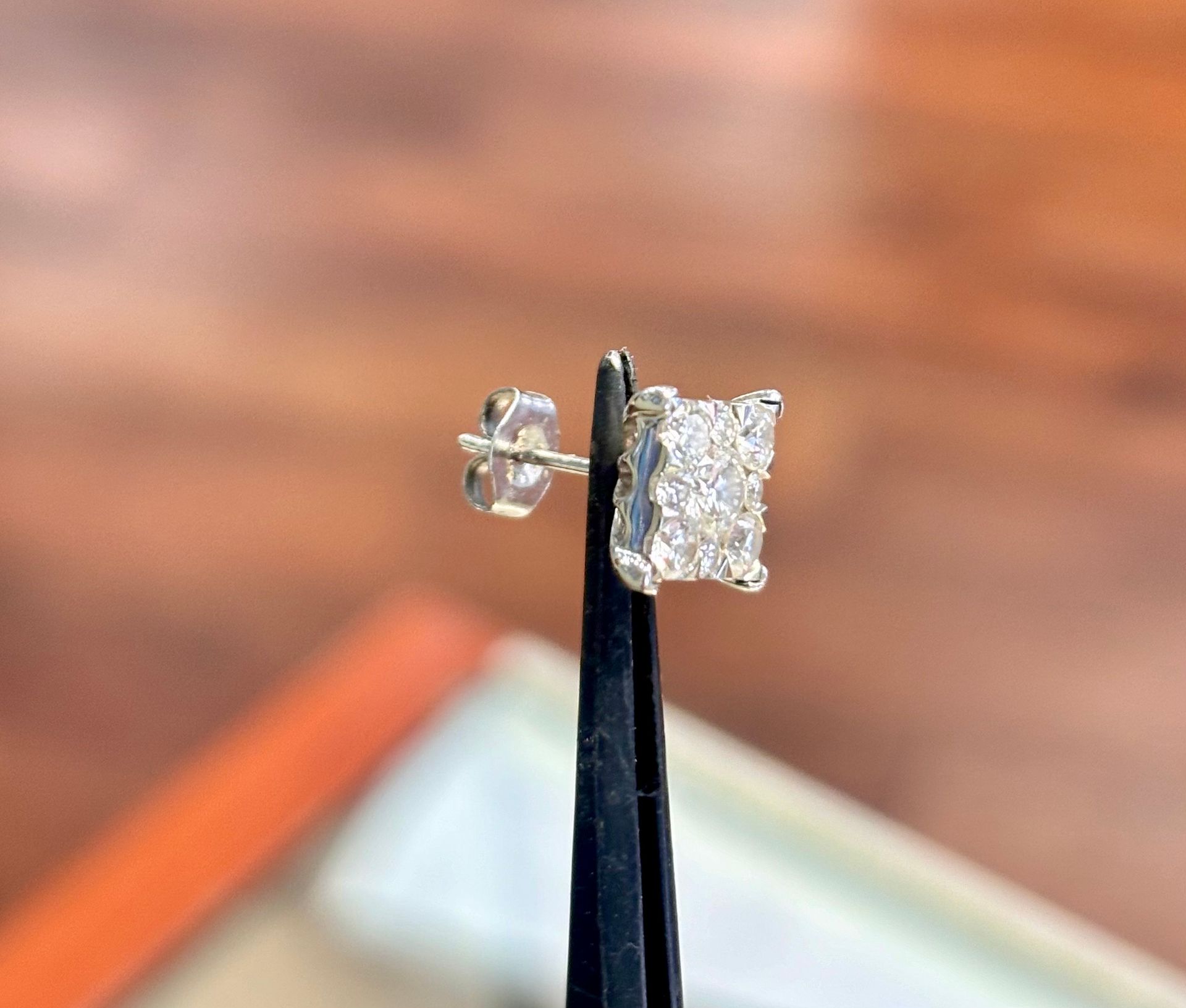 A pair of diamond stud earrings sitting on top of a pair of tweezers.