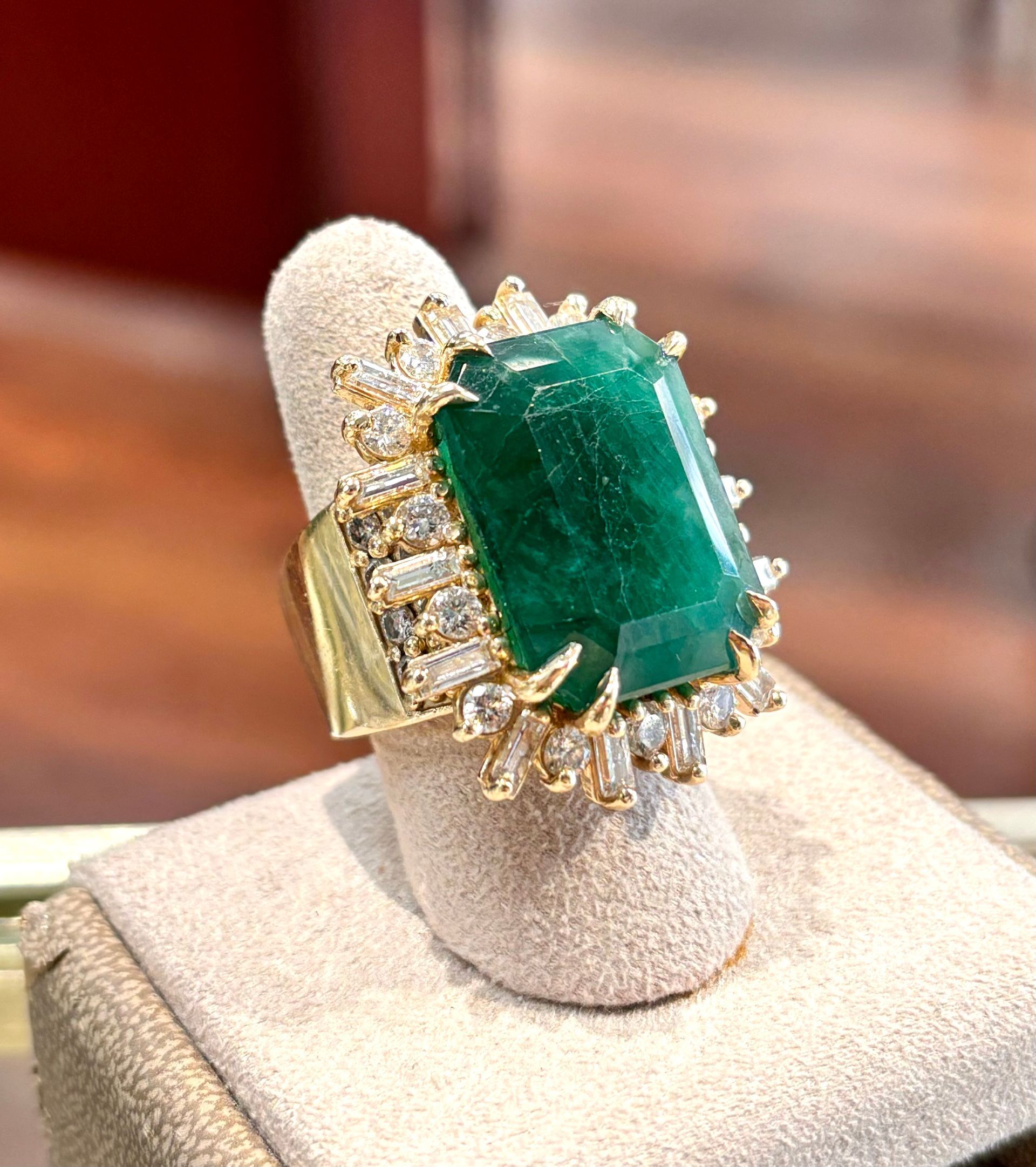 A close up of a ring with an emerald and diamonds on a finger.