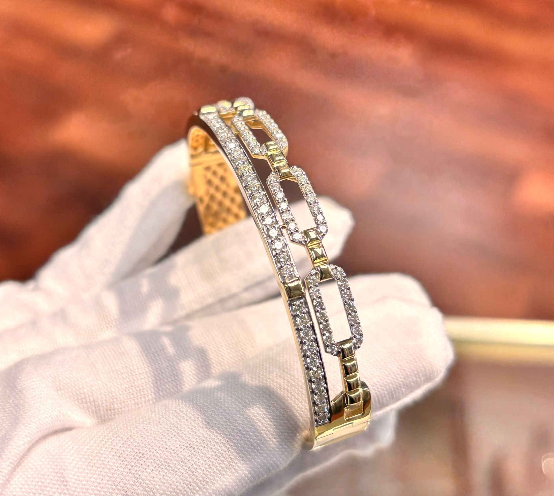A person wearing white gloves is holding a gold and diamond bracelet