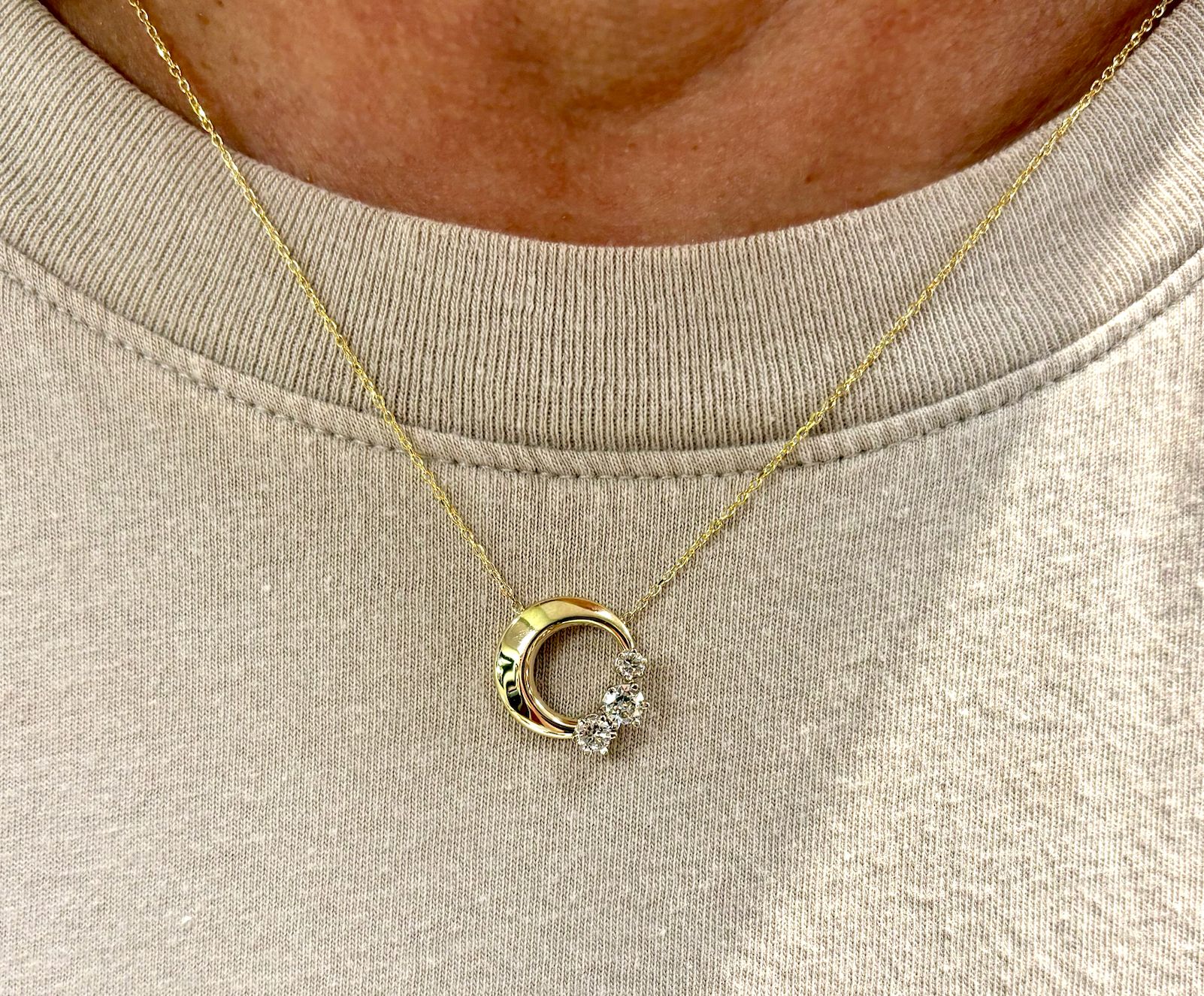 A woman is wearing a necklace with a crescent moon pendant.