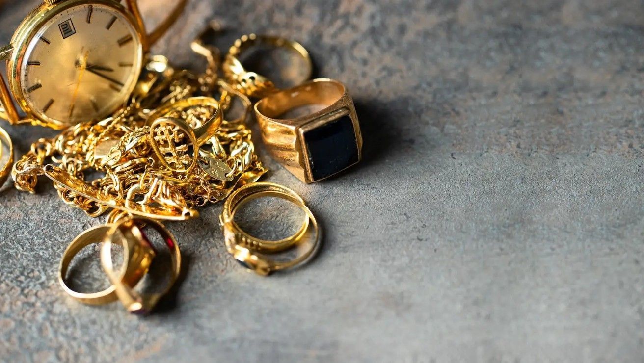 A pile of gold jewelry including a watch and rings on a table.
