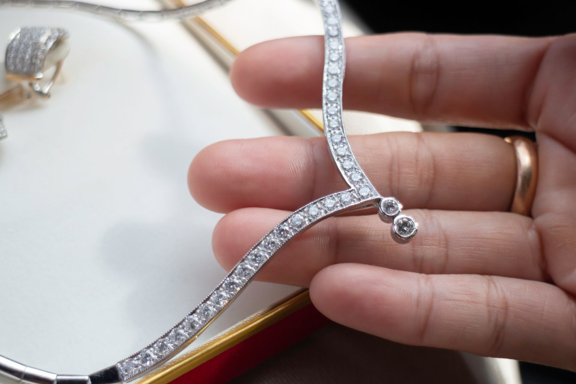 Person's hand holding a diamond necklace with a curved design, set on a white surface.