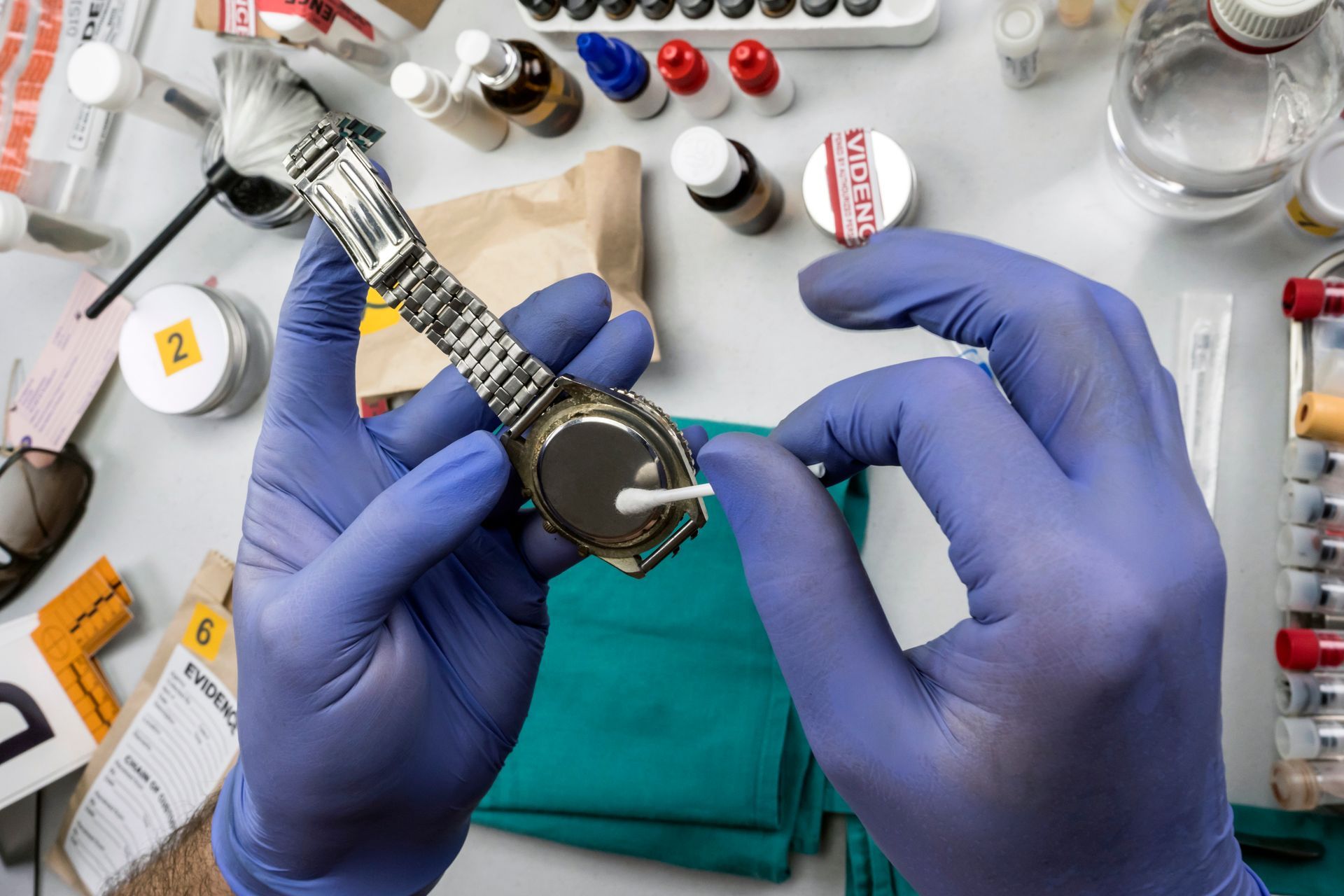 A person wearing blue gloves is cleaning a watch with a cotton swab.