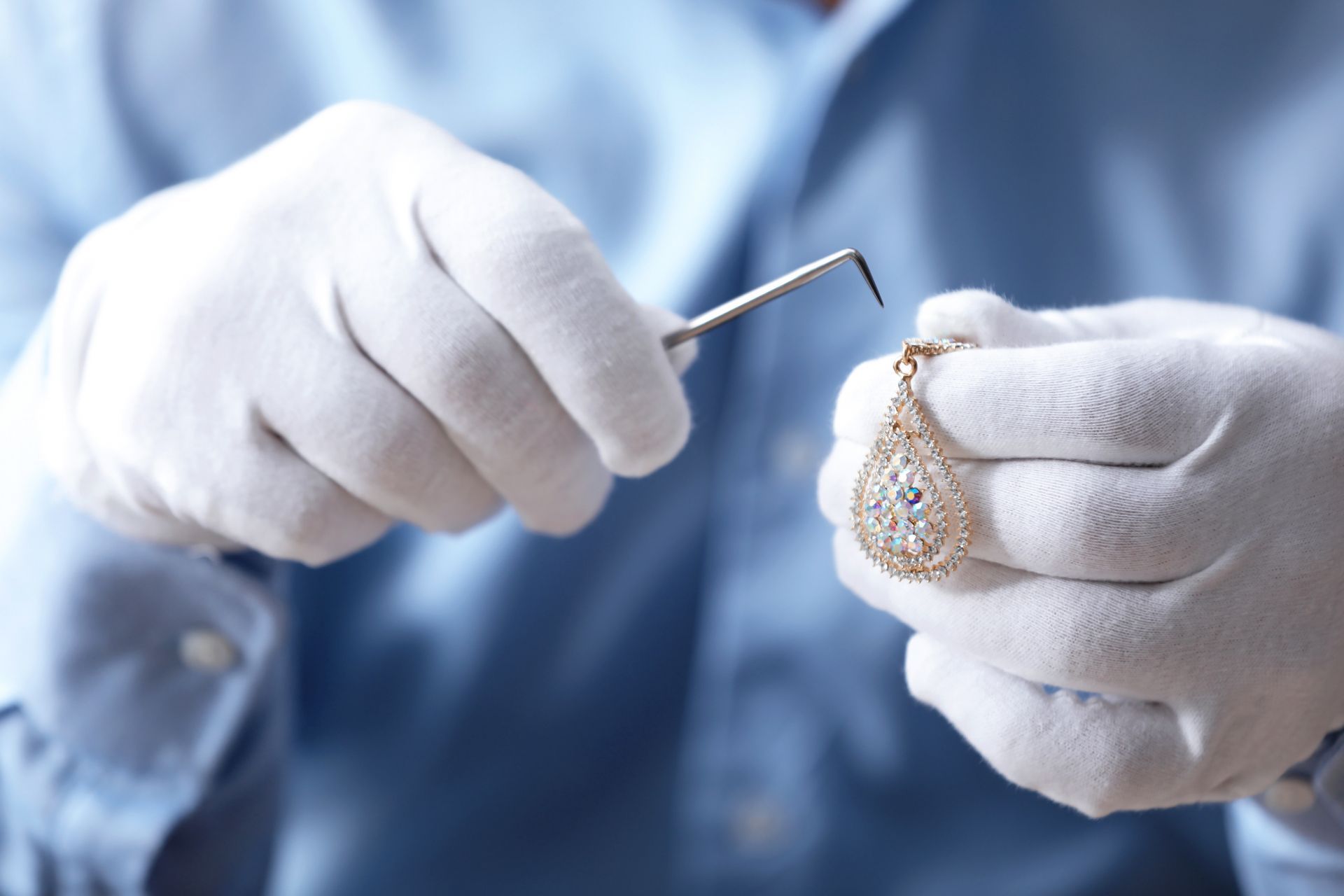 Person in gloves examining a gold pendant with a tool.