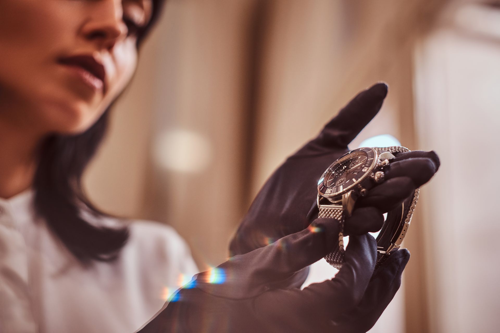 Woman in black gloves inspecting a luxury watch, indoor setting, soft lighting.