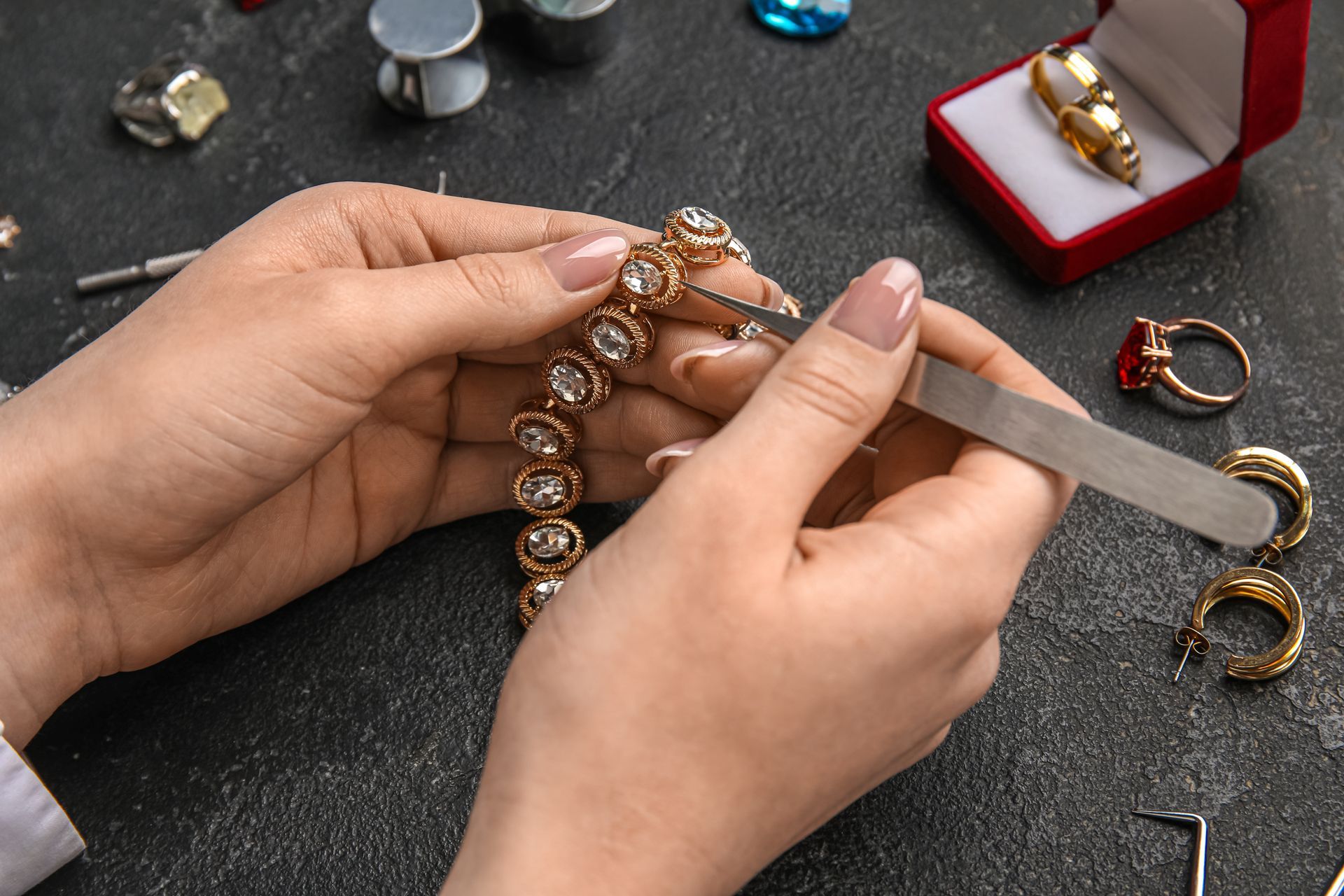 A woman is working on a bracelet with a pair of tweezers.