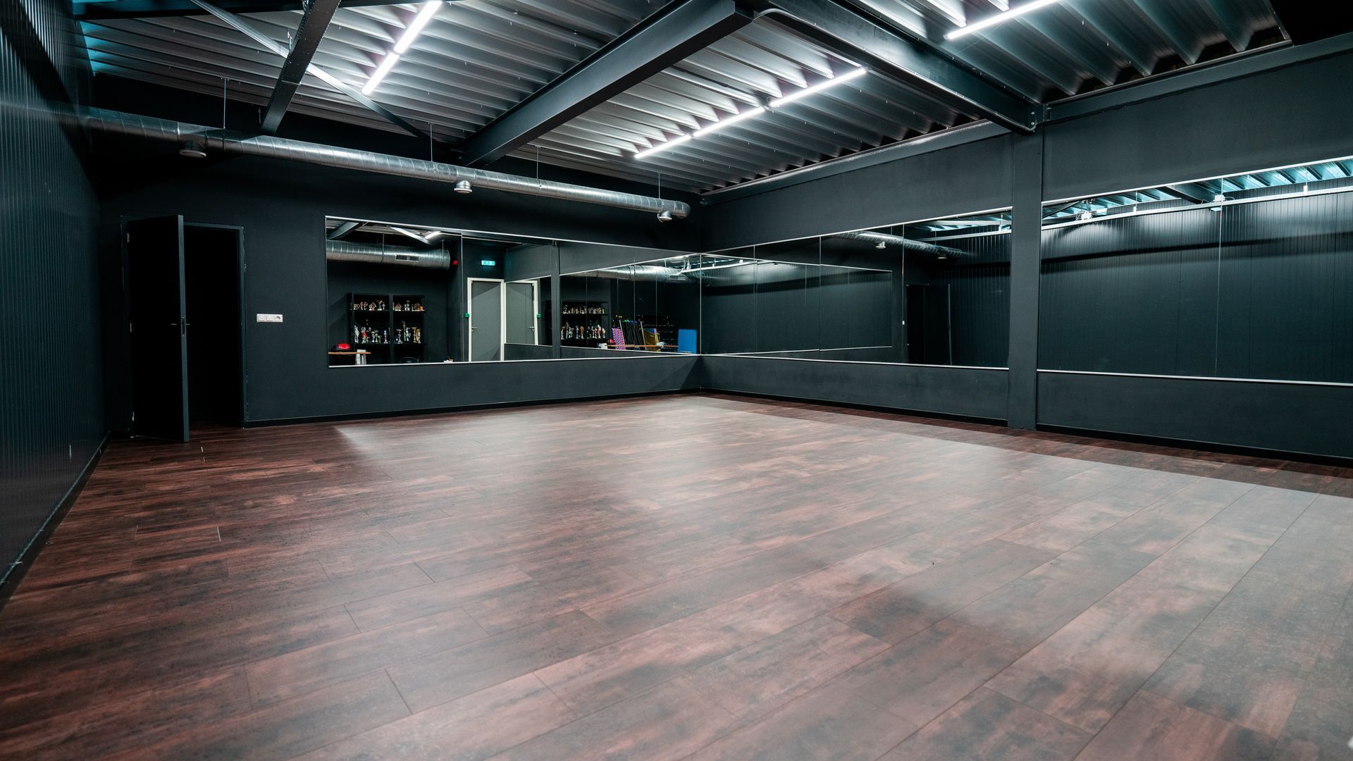 Een grote lege dansstudio met houten vloeren en spiegels.