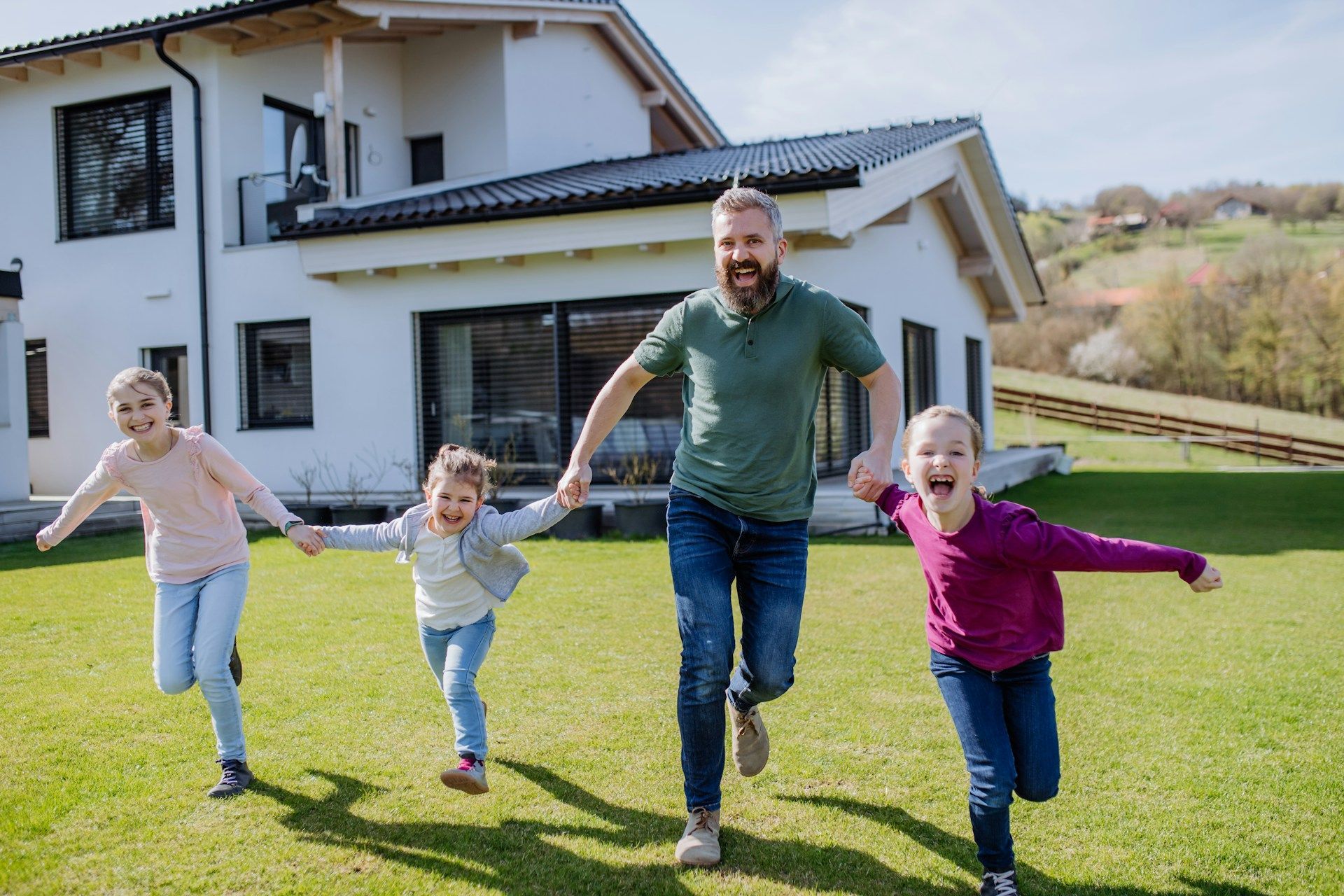 A man and three children are running in front of a house.